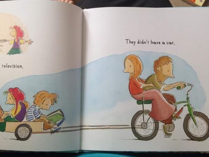 On the pages of a children's book, we can see a family where the parents are riding on a single bike, pulling their children behind in a trailer. The children are reading. 