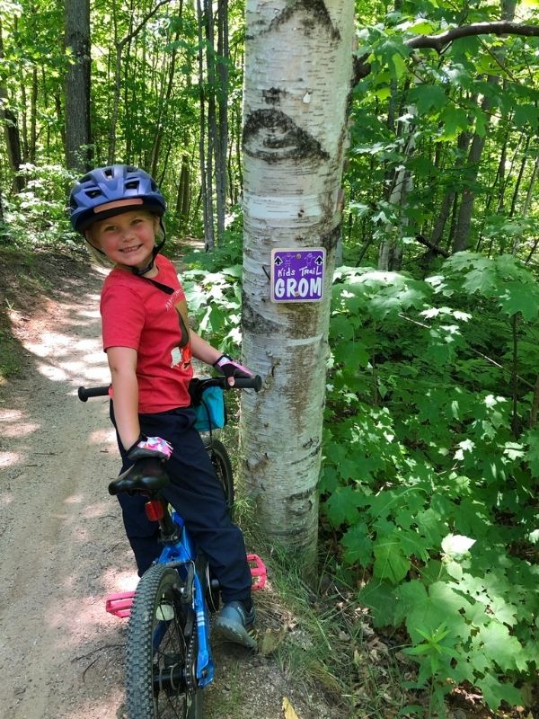 Girl on Prevelo Alpha Two Bike next to a birch tree with a purple Grom sign.