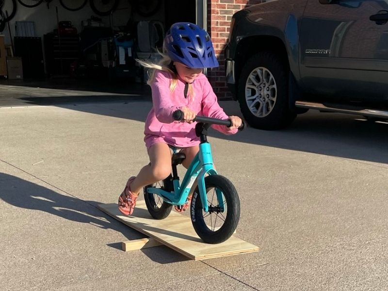 Girl rides Hornit Airo balance bike over a homemade teeter.