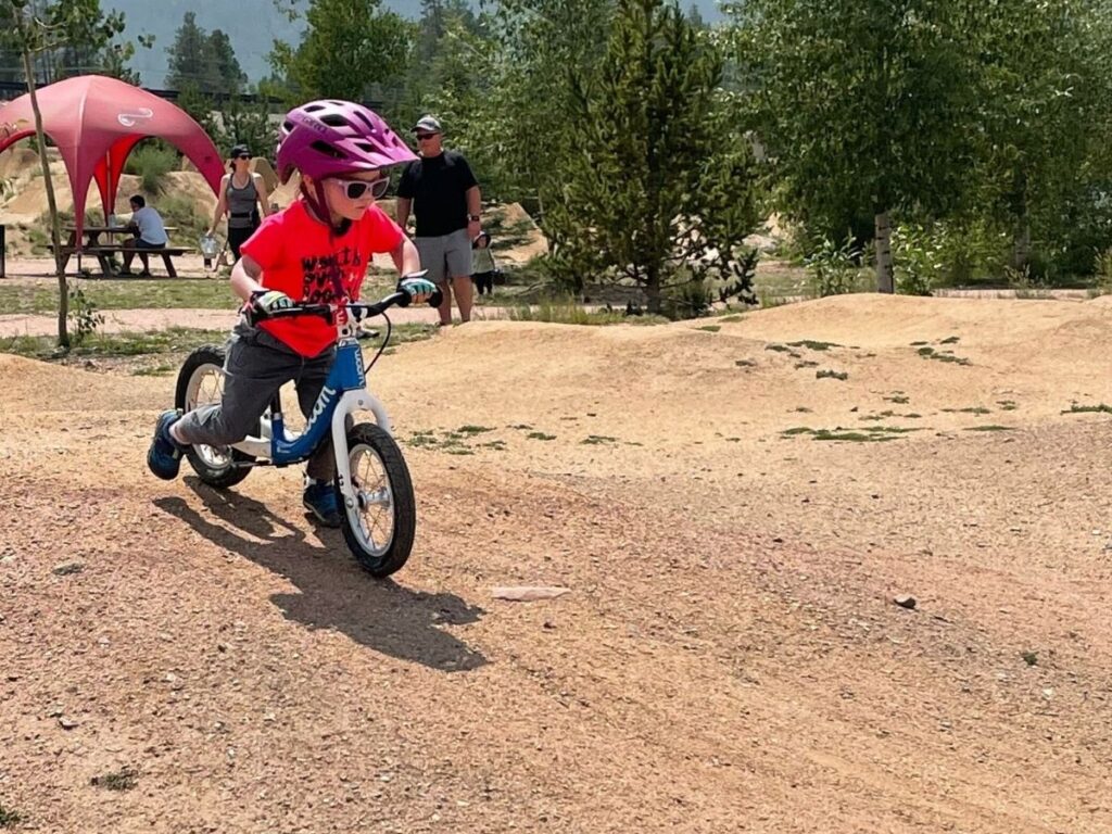 Child speeds down a dirt hill on his Woom bike.