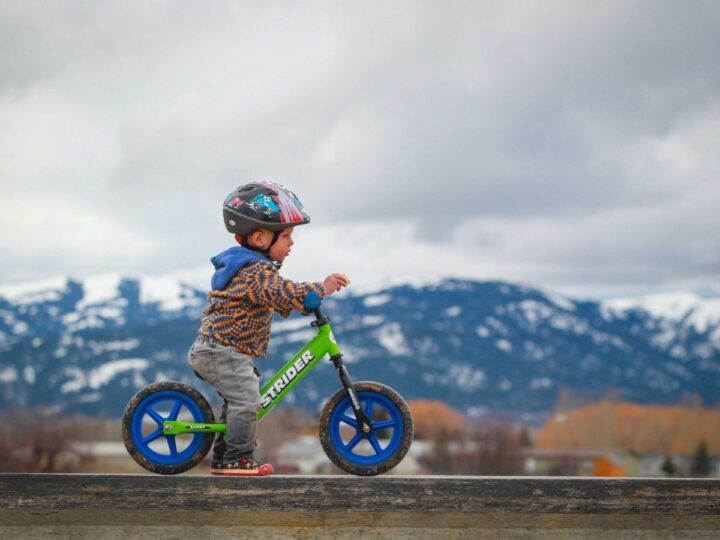 Little boy rocking balance bike at bike park near mountains. 