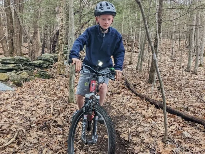 A boy rides with bike light through a leafy path.