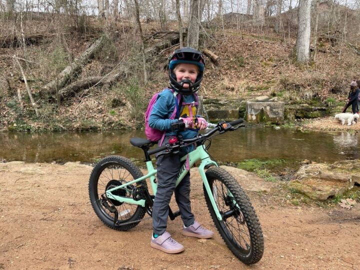 Girl standing over her Specialized Riprock bike with a river behind her.