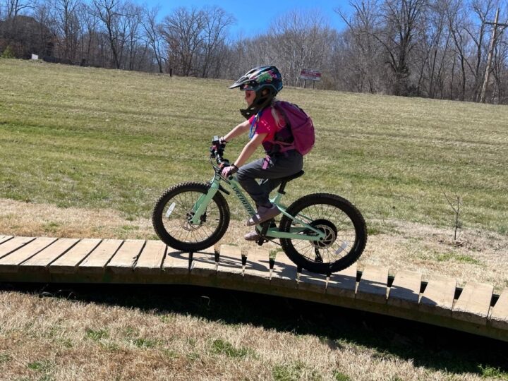Girl riding her bike over a wooden bike bridge.