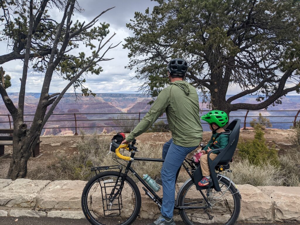 A dad rests on his bicycle with a child in a rear seat.