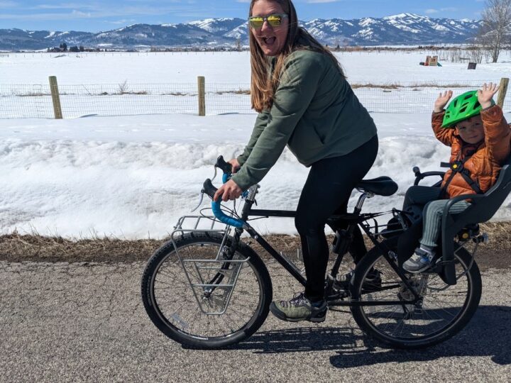 A woman rides a bike with a toddler in a bike seat