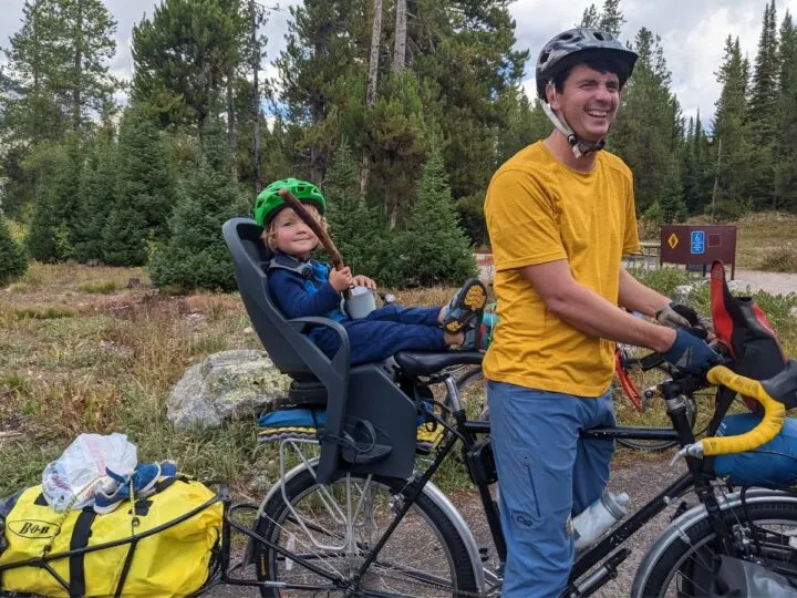 a toddler kicks his feet up behind his dad from  rear bike seat.