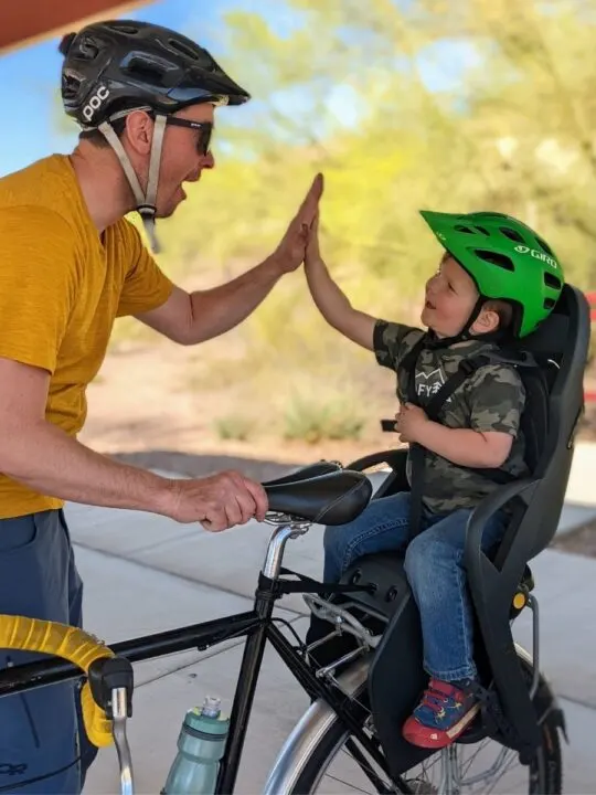 A dad and toddler high five while on a bike break.