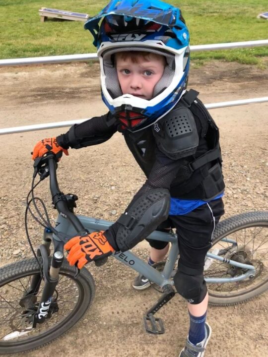 photo of a child standing over his bike wearing a full-face helmet, protective padding, and bike gloves