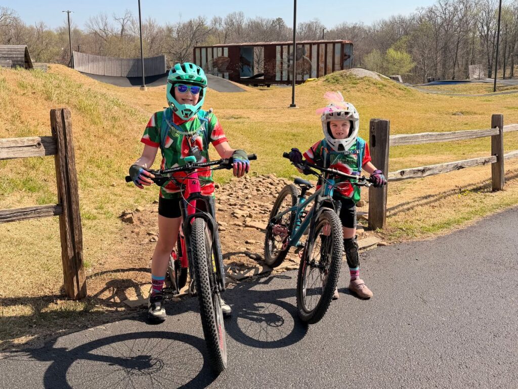 FullFaceHelmet6 Two girls with watermelon jerseys and full face helmets stand in front of a bike park.