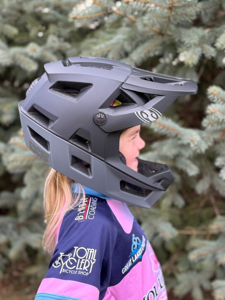 A young girl stand sideways with an IXS Full Face Trigger helmet on.