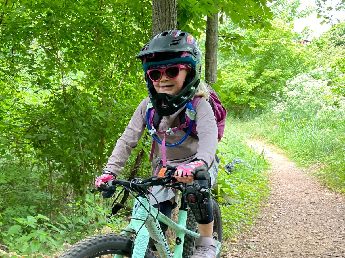 A young girl wearing a full face bike helmet is riding a mint specialized bike on a trail.