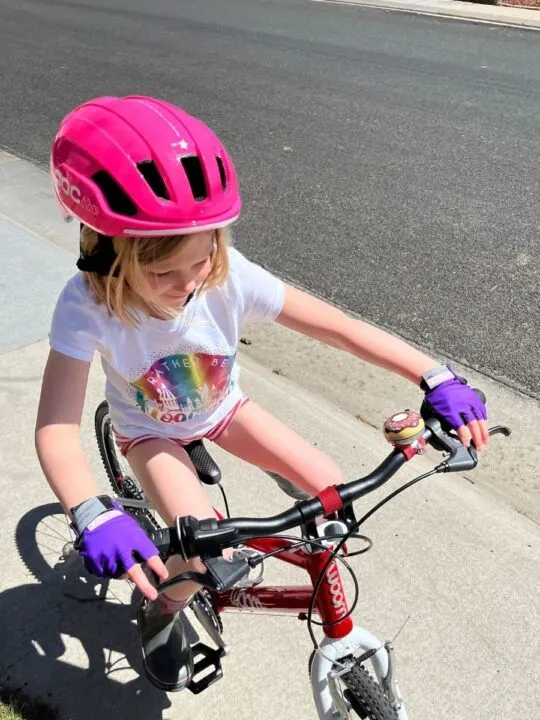 photo of a child riding her bike wearing a bike helmet and Aerotech Designs half-finger bike gloves