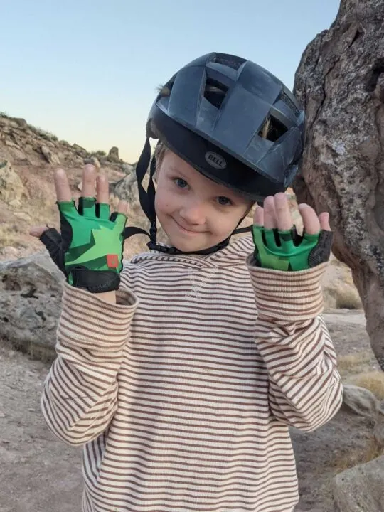 photo of a child smiling and wearing a bike helmet and bike gloves