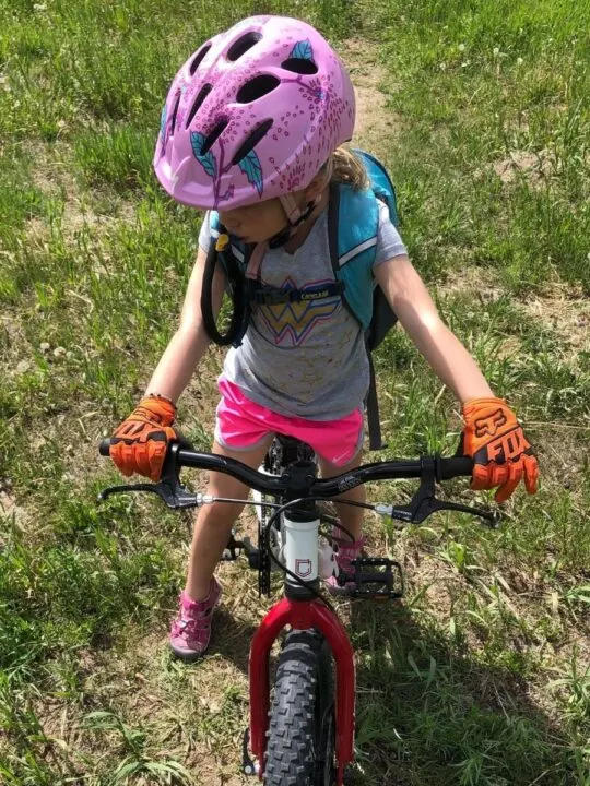 photo of a child standing over her bike wearing a helmet and bike gloves