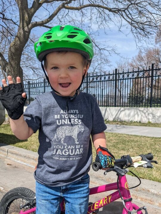 photo of a young child wearing a bike helmet and bike gloves standing next to his bike