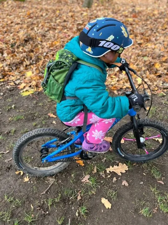 photo of a child riding a bike wearing a bike helmet and Woom Warm Tens bike gloves