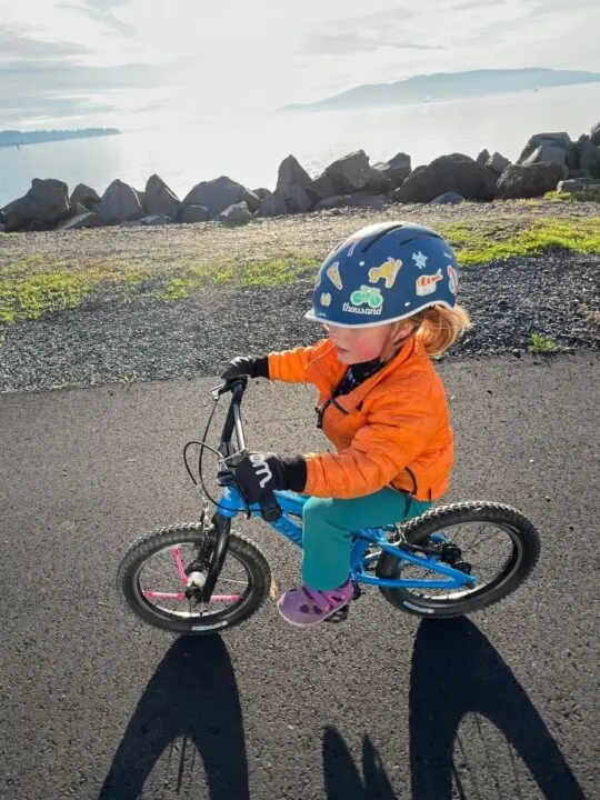 photo of a child riding a bike on a path and wearing a bike helmet and bike gloves