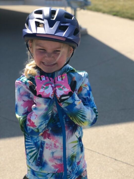 photo of a child smiling and wearing a bike helmet and ZippyRoos half-finger bike gloves