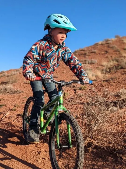 photo of a child wearing a bike helmet and bike gloves riding a bike in the desert