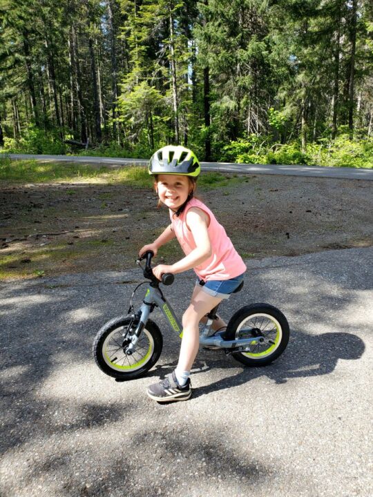 five year old girl smiling sitting on balance bike