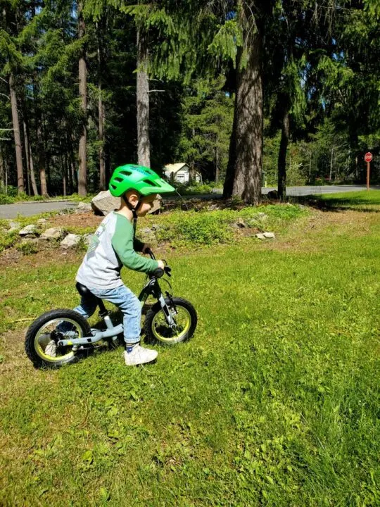 little boy riding his balance bike through grass