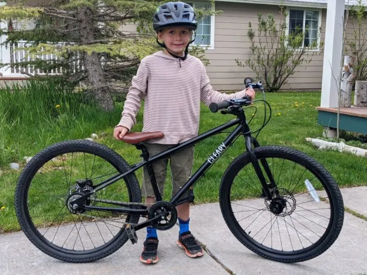 A young boy poses with a black bicycle.