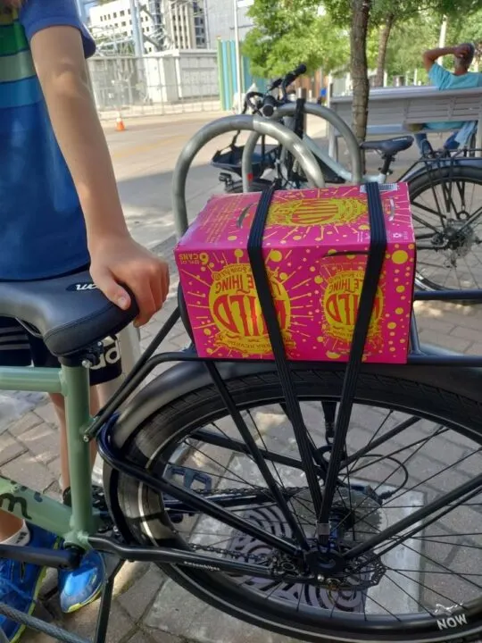 A pink and yellow six-pack of beer sits securely on a kids' bike rack. 