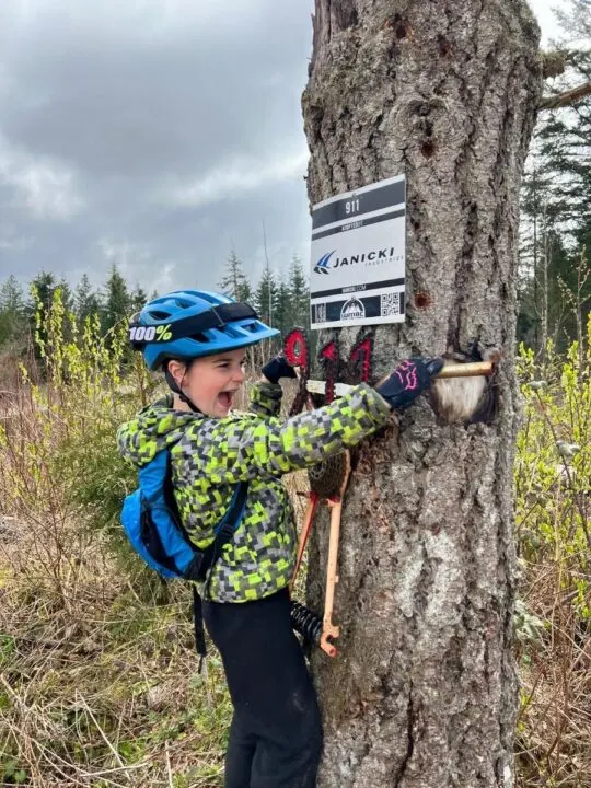 photo of a child standing next to a tree and holding onto a metal trail sign reading "911"