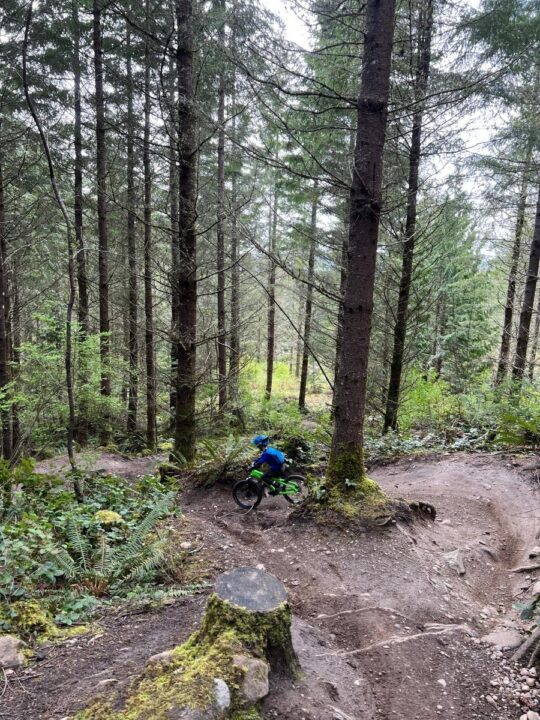 Photo of a child riding a mountain bike down a dirt trail in the woods
