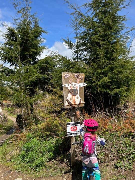 Photo of a child ringing the bell hanging from the trail sign for the Cow Belle trail on Galbraith Mountain