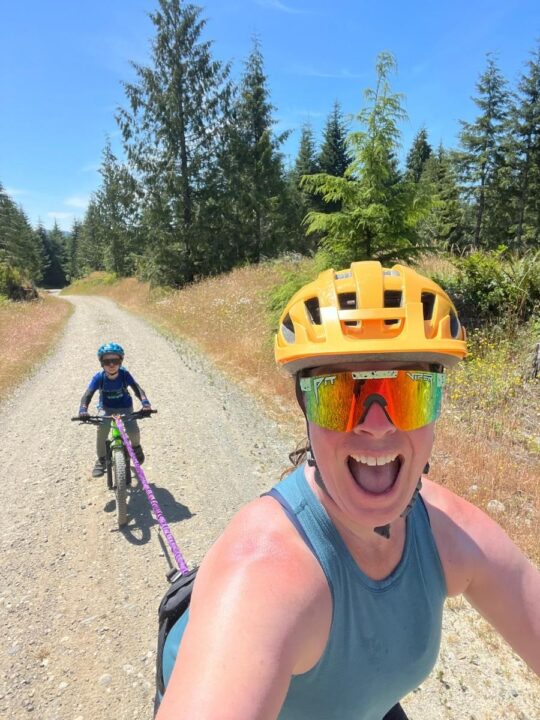 Photo of an adult on a bike towing a child on a bike up a gravel road