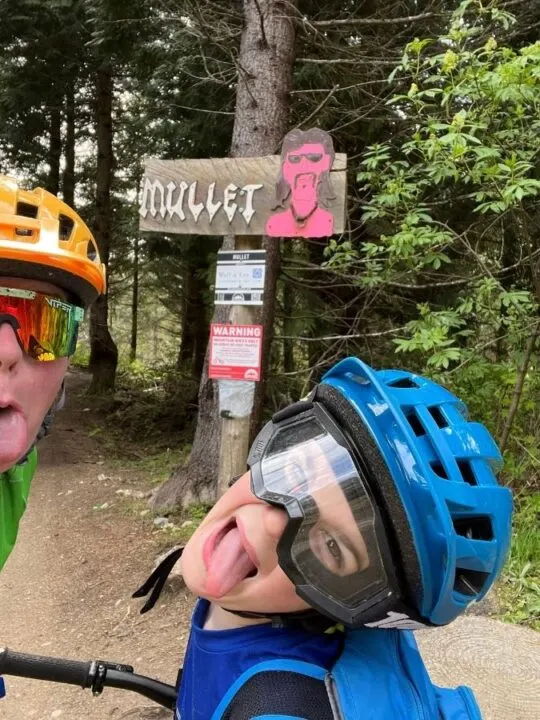 photo of two people sticking their tongues out in front of a trail sign reading "Mullet"