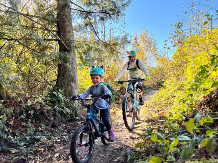 photo of a father and daughter riding bikes down a singletrack trail. Best family biking in Bellingham.