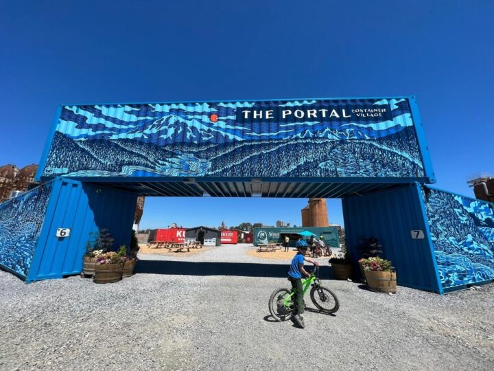 Photo of a child on a bike in front of an arrangement of shipping containers with a mural on it