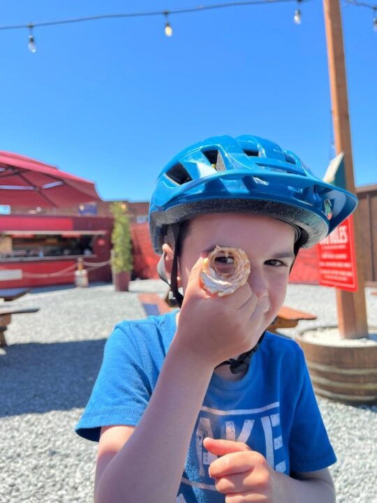 Photo of a child wearing a bike helmet and looking at the camera through a hole in the bottom of an ice cream cone