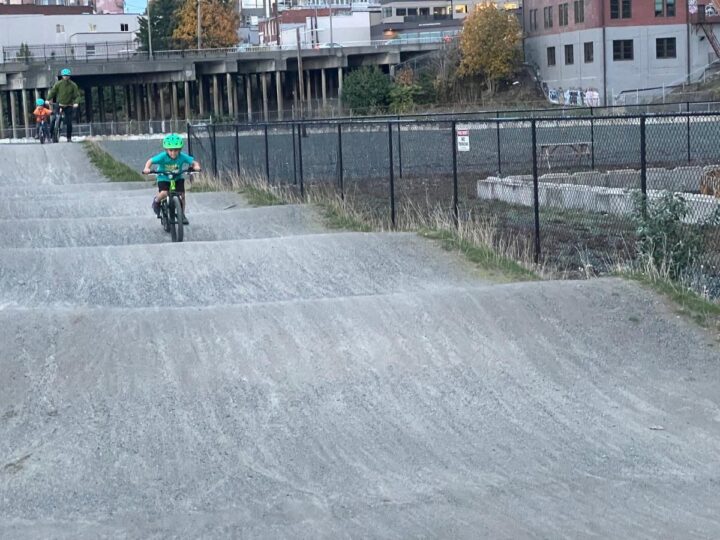 photo of child riding a bike on a dirt pump track in bellingham, WA.