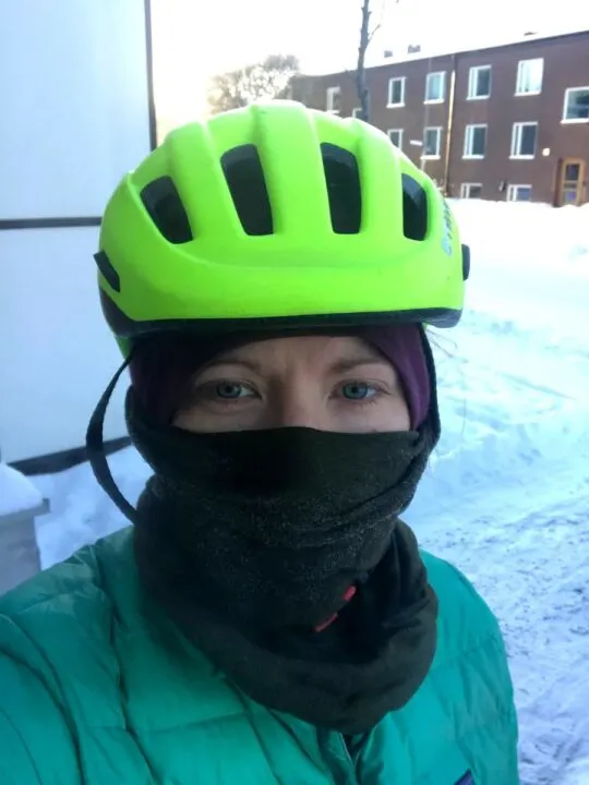 a selfie of a woman in a bright yellow helmet and face half-covered with a wool tube. it's snowing