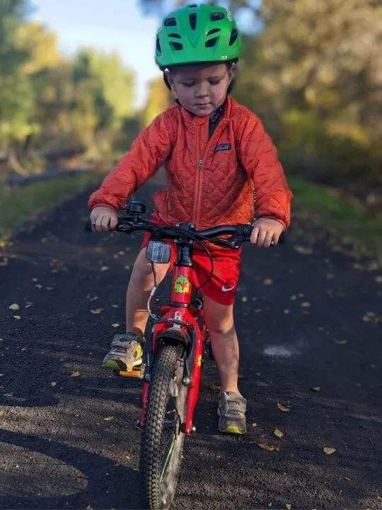 A little boy sits atop a little red bike, testing the brakes and pedals.
