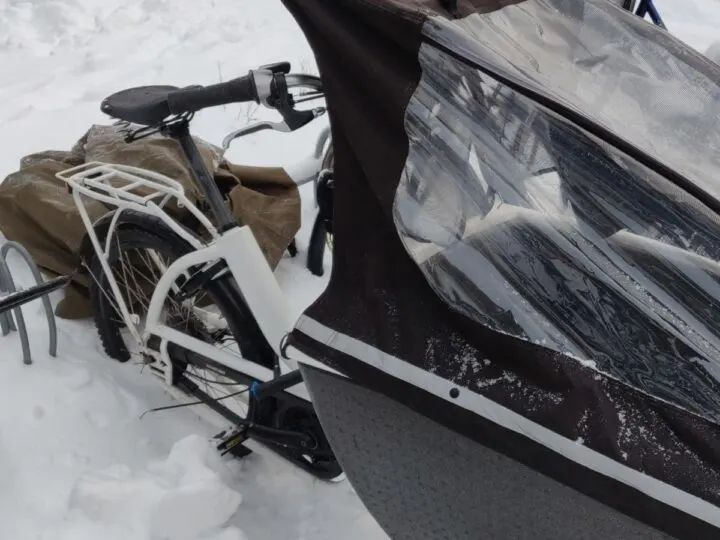A cargo bike with raincover sits in a couple feet of snow on an outdoor bike rack