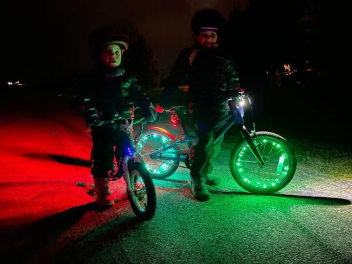 Two kids ride bikes with bright wheel lights