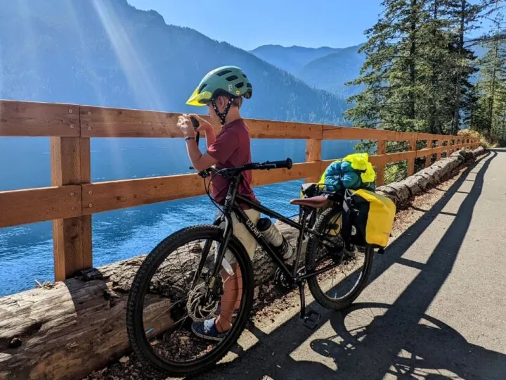 A boy takes a picture along a lakeside trail with his bike.