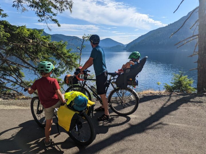A dad and two kids look out over a lake from their bikes.