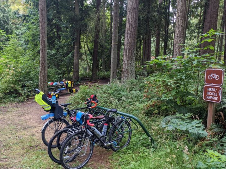 Bikes parked on a rack next to a campsite in the woods.