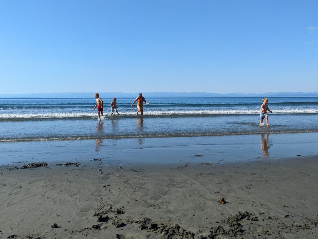 A mom and three kids run around in small waves on a beach.