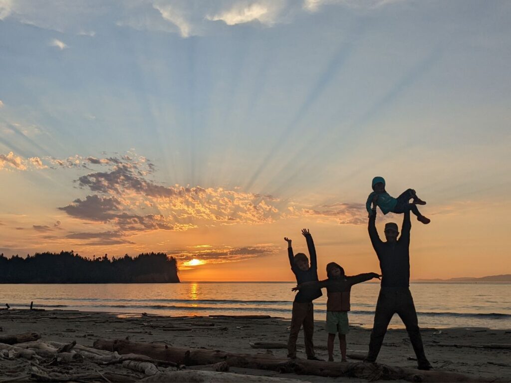 A dad and three kids silhouetted against an orange sunset