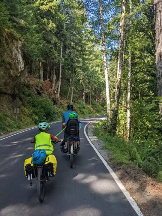 A dad tows his sons up a hill on bicycles.