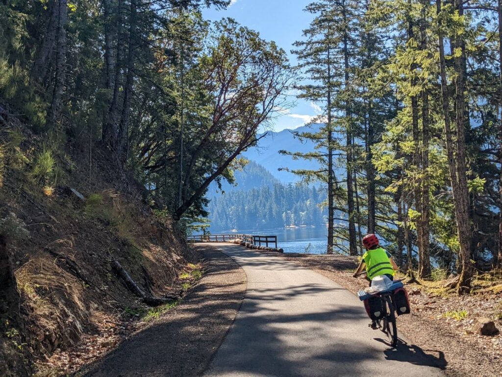 A boy rides his bike on a path along a mountain lake