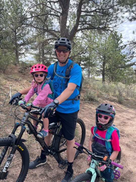 Dad with two girls mountain biking wearing Osprey hydration packs.