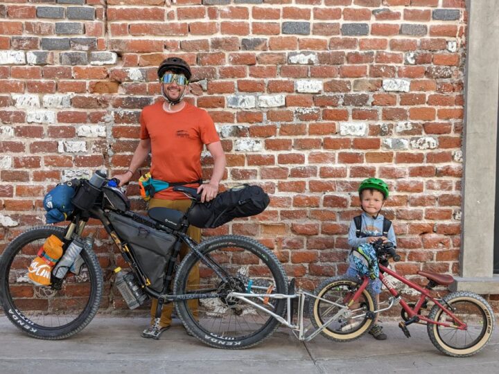 A dad and child pose in with loaded bikes connected by a follow-me-tandem. FollowMe Tandem Review
